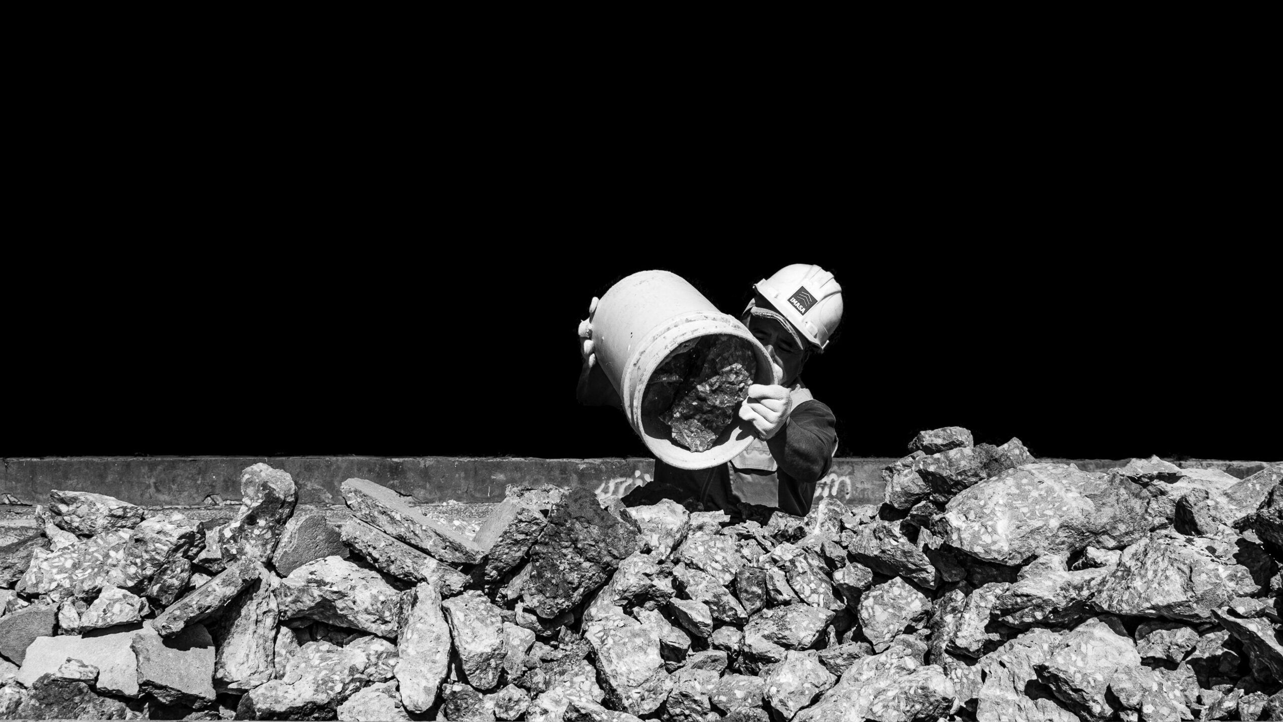 Construction worker in hard hat handling rocks, monochromatic urban setting.