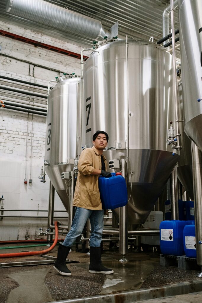 Asian man managing fermentation tanks in a brewery, highlighting craft beer production.